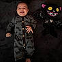 baby, bat_pattern, black_background, child, costume, cute, dark_colors, happy, indoor, infant, infant_clothing, lying_down, onesie, playful, plush, portrait, smiling, soft_texture, stuffed_toy, toy