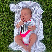 Oaklynn is registered to the contest to win money with this photo: baby, infant, grass, outdoor, towel, onesie, nike, clothing, hand, foot, person, newborn, skin, cute, lying, daylight, nature, young_child, relax, casual