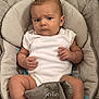 baby, infant, child, onesie, seat, baby_carrier, cushion, face, expression, curious, neutral_colors, skin, hand, foot, indoor, young_child, person, portrait, clothing, comfort