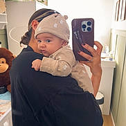 Zayn joined the competition — help win amazing prizes! baby, adult, mirror, selfie, phone, hat, plush_toy, nursery, room, person, clothing, hand, furniture, wall, decor, child, holding, portrait, indoor, soft_light
