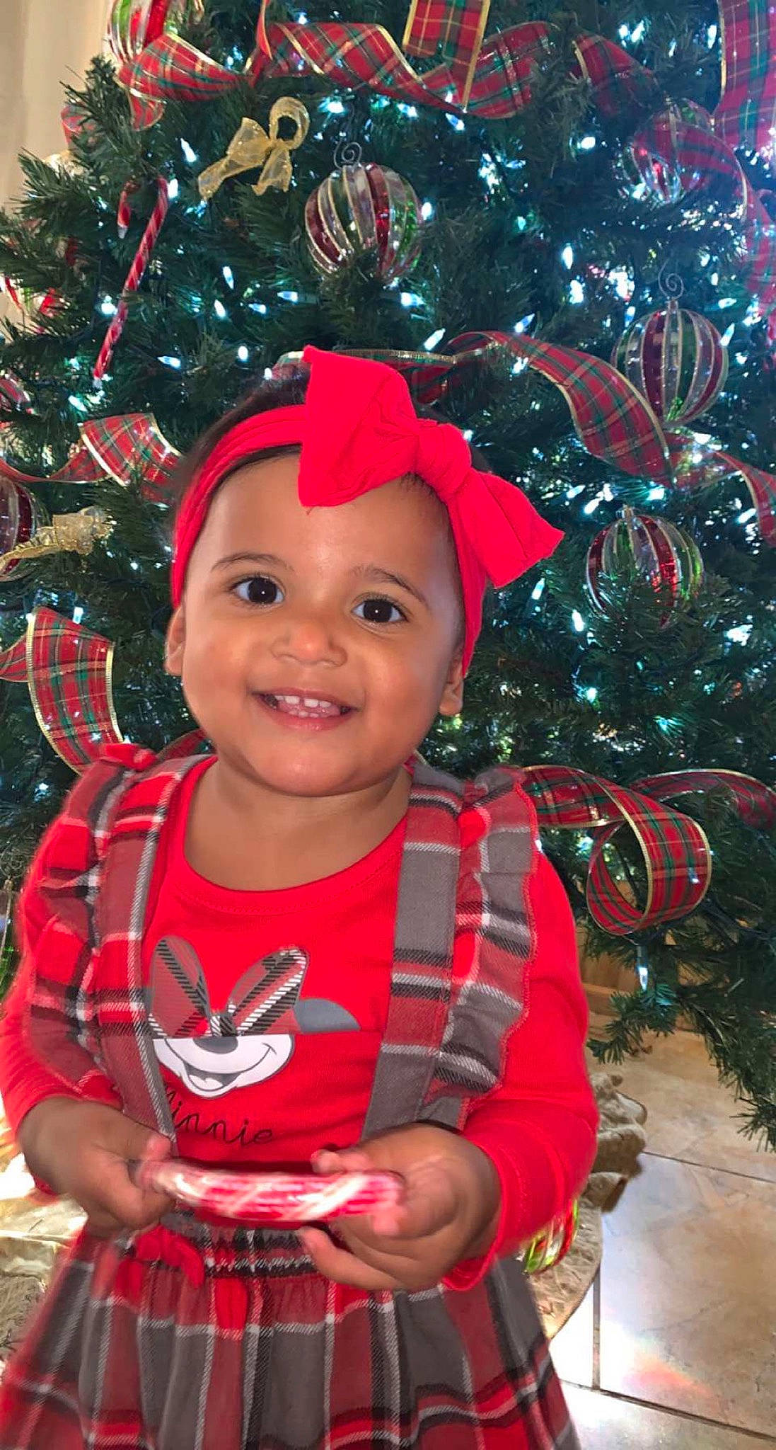 Hallie Rae is registered to the contest to win money with this photo: baby_toddler_clothing, branch, christmas_ornament, christmas_tree, face, facial_expression, fun, happy, head, headgear, headwear, holiday_ornament, human_body, joy, leaf, people_in_nature, person, pink, plant, red