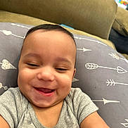 Kaiden is registered to the contest to win money with this photo: baby, smiling, infant, pillow, arrows, hearts, clothing, gray_shirt, cute, happy, face, child, indoors, closeup, person, skin, head, expression, joy, young