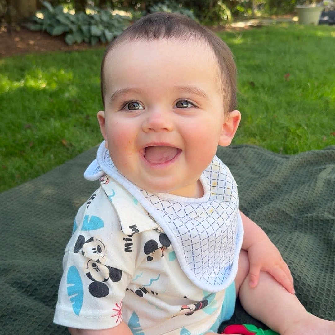 Declan joined the competition — help win amazing prizes! baby, bib, blanket, cheerful, child, cute, daylight, face, grass, greenery, happy, infant, mickey_mouse, nature, outdoor, portrait, shirt, sitting, smiling, sunlight