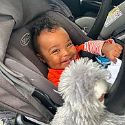 Zhyaire is registered to the contest to win money with this photo: baby, car_seat, smile, child, toy, stuffed_animal, gray, orange_clothing, infant, seatbelt, happy, car_interior, person, cute, plush, portrait, young_child, curly_hair, indoors, playful