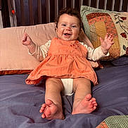 Ashton is registered to the contest to win money with this photo: baby, child, smiling, sitting, bed, pillow, blanket, clothing, happy, face, feet, hands, curly_hair, indoor, person, cute, young_child, furniture, textile, portrait