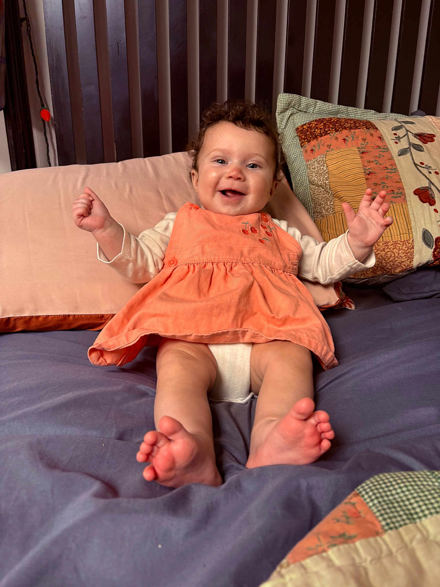 Ashton is registered to the contest to win money with this photo: baby, child, smiling, sitting, bed, pillow, blanket, clothing, happy, face, feet, hands, curly_hair, indoor, person, cute, young_child, furniture, textile, portrait