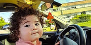 Joud a rejoint le concours — aidez-le/la à gagner de superbes lots ! toddler, child, car, steering_wheel, curly_hair, pink_shirt, hands, adult_hand, inside_car, window, daylight, greenery, building, parked_car, seat, dashboard, rearview_mirror, cute, portrait, helping_hand