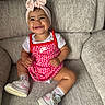 baby, child, smiling, headband, pink_bow, nike, dress, sneakers, socks, couch, furniture, indoor, happy, cute, portrait, seated, apparel, footwear, person, infant