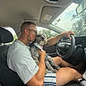 Paul Anka joined the competition — help win amazing prizes! man, dog, car_interior, driving, pet, love, affection, casual_clothing, glasses, bandana, shorts, steering_wheel, window, seat, nature, trees, daytime, portrait, human_animal_interaction, transportation