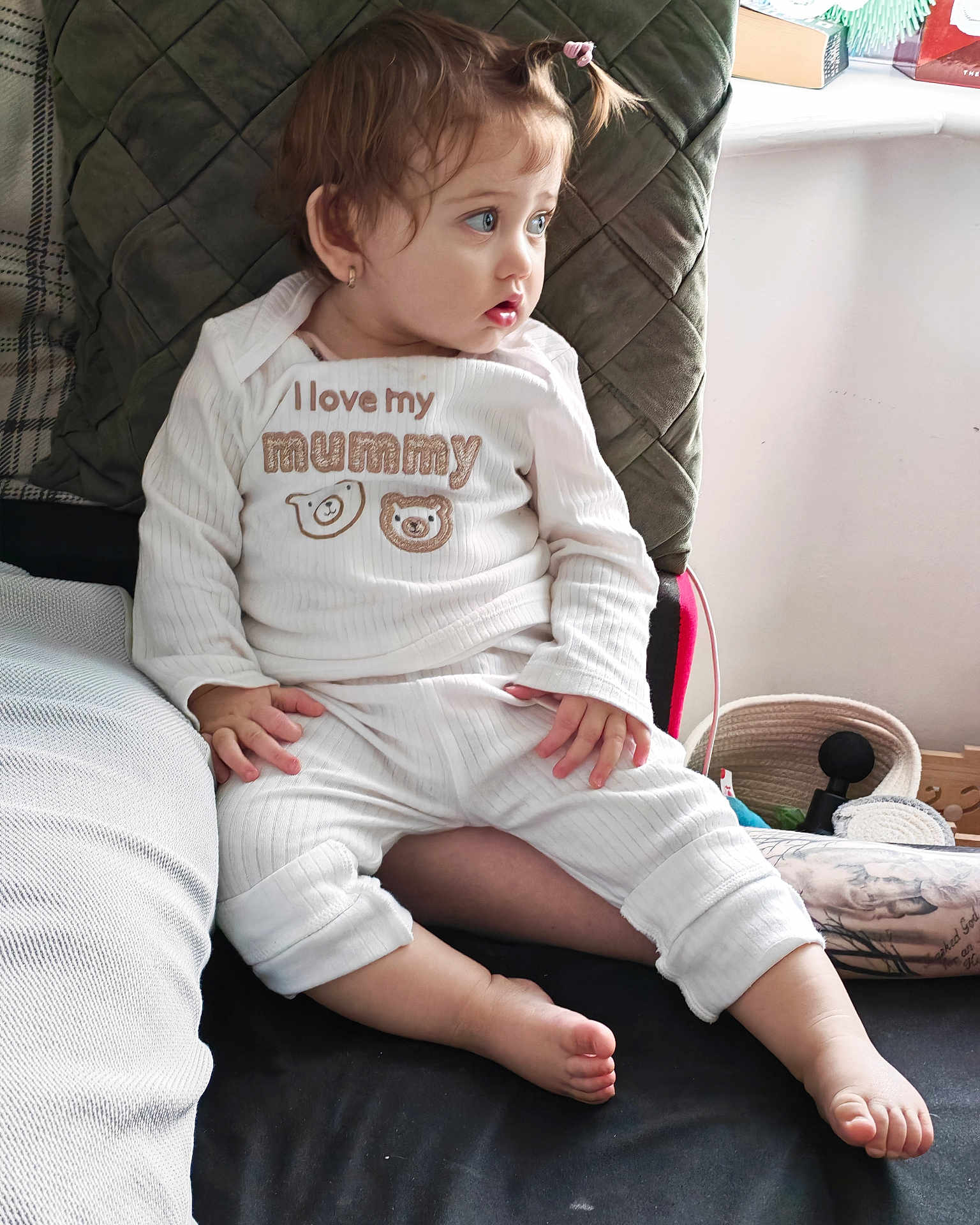 Georgiana is registered to the contest to win money with this photo: toddler, child, pajamas, white_clothing, sitting, couch, cushion, indoor, curly_hair, pony_tail, barefoot, face, looking_away, home, comfort, cute, expression, small_hands, young_child, cozy