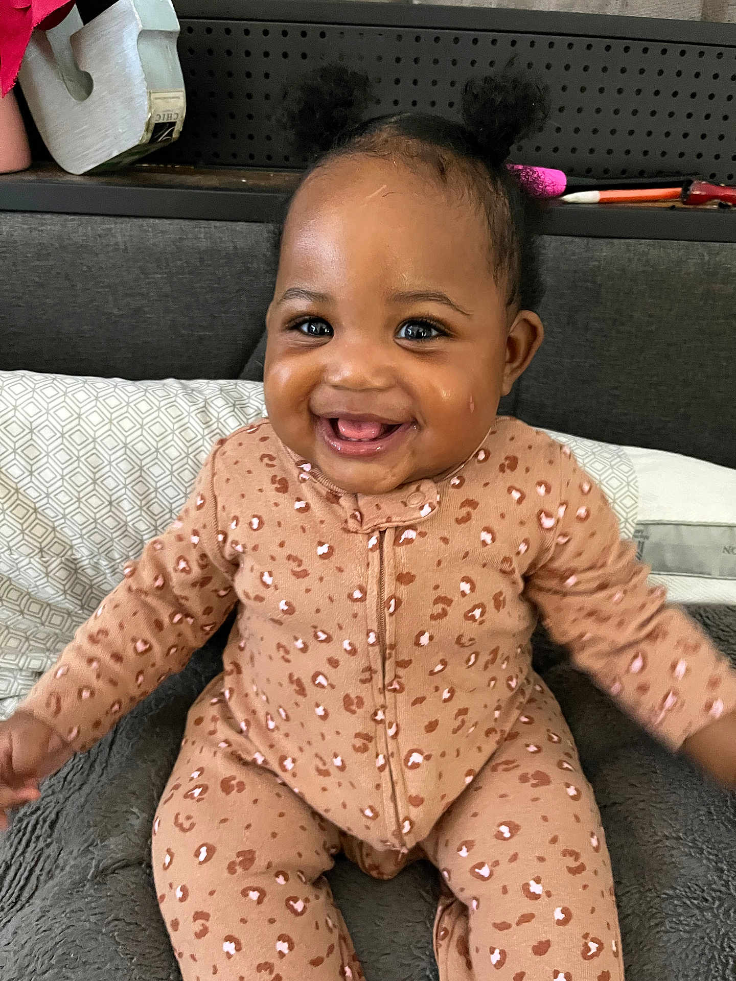 Avery joined the competition — help win amazing prizes! baby, infant, smiling, happy, cute, child, onesie, leopard_print, hair_buns, indoor, bed, pillow, blanket, face, person, skin, expression, joy, seated, comfort