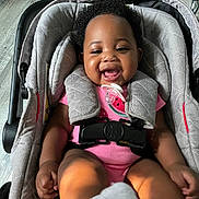 Avery is registered to the contest to win money with this photo: baby, smiling, car_seat, pink_clothing, pacifier, curly_hair, indoor, wooden_floor, happy, child, infant, foot, sock, seatbelt, cushion, black_hair, cute, playful, person, portrait