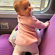 Manon a rejoint le concours — aidez-le/la à gagner de superbes lots ! baby, child, pacifier, pink_sweater, white_tights, purple_seat, train, window, rain, climbing, curious, indoor, seat, travel, infant, candid, face, person, looking_back, cozy