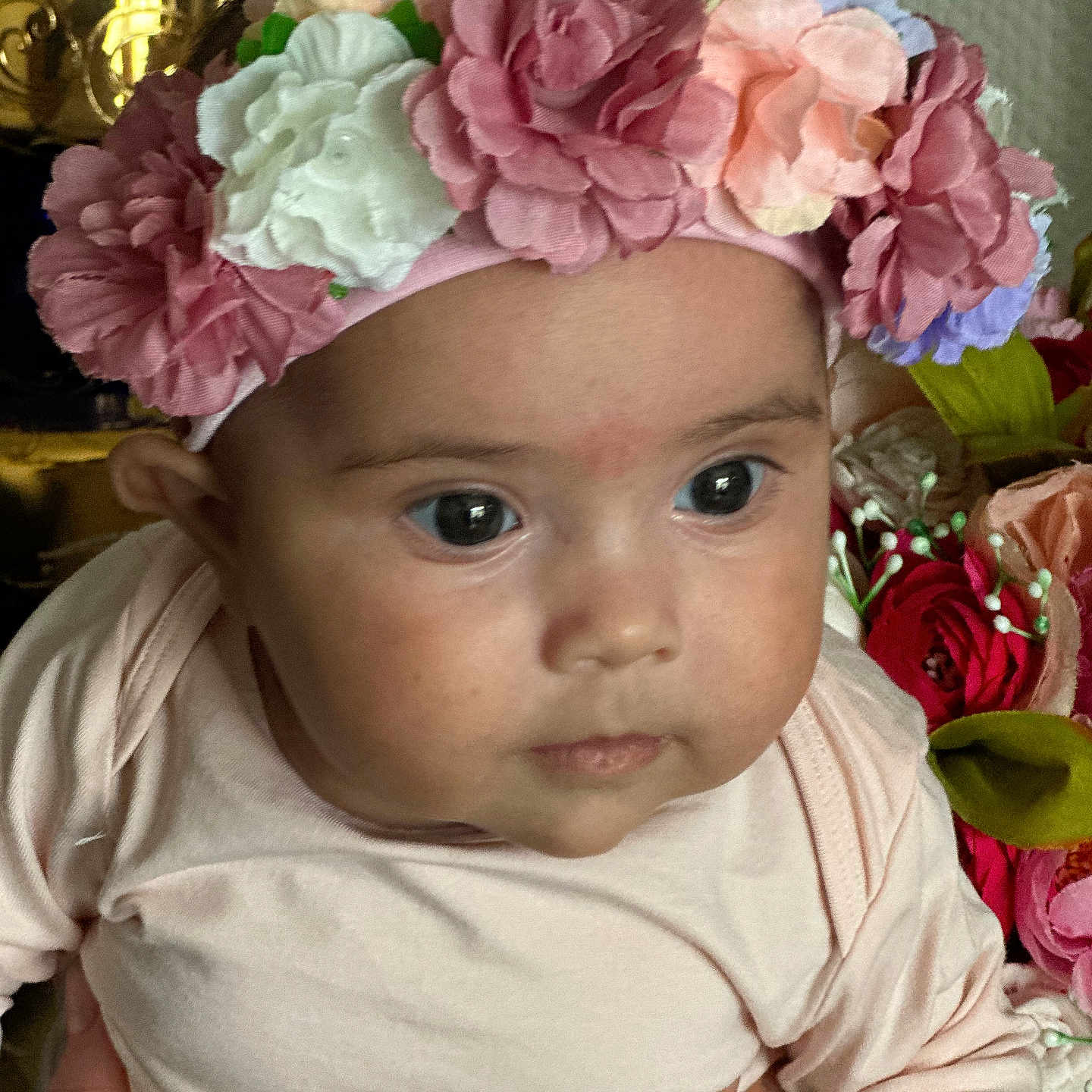 Amélie participe au concours pour gagner de l'argent avec cette photo : baby, flower_headband, pink_clothing, close_up, hand, face, eyes, infant, portrait, curious, skin, artificial_flowers, floral, background, person, child, cute, soft_lighting, indoors, head