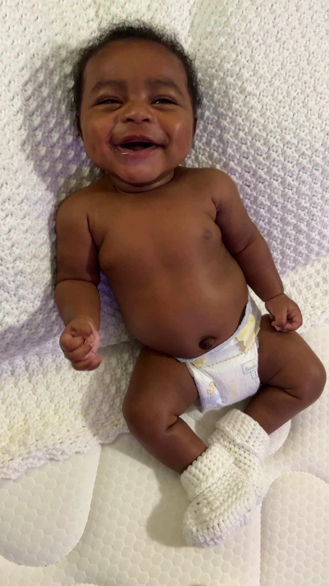 Samir Baldwin joined the competition — help win amazing prizes! baby, smiling, diaper, blanket, knitted_booties, infant, cute, happy, lying_down, skin, child, one_person, indoors, soft_texture, face, newborn, toddler, human, comfort, sweet