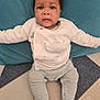 baby, child, infant, pajamas, striped_clothing, whale_design, floor, cushion, teal, patterned_floor, person, indoors, seated, footed_pajamas, cute, young_child, face, looking_at_camera, long_sleeves, comfort