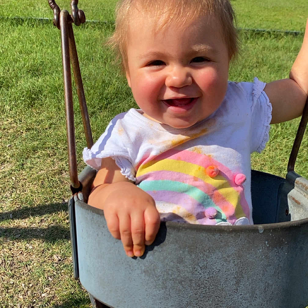 Noelle is registered to the contest to win money with this photo: toddler, child, baby, smiling, happy, swing, playground, outdoor, grass, sunlight, portrait, face, person, park, fence, bench, pool, summer, clothing, rainbow