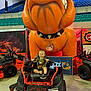 toddler, child, lawn_mower, orange, inflatable, dog, toy, indoor, event, seat, smile, machine, vehicle, spikes, collar, bleachers, sign, floor, person, casual