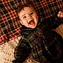 baby, child, infant, smile, open_mouth, happy, plaid, blanket, pillow, bedding, pattern, dress, clothing, portrait, face, eyes, hair, indoor, cozy, texture