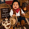 baby, child, cowboy, hat, boots, bandana, vest, cake, candle, sign, texas_flag, lantern, wood, rope, carpet, smiling, sitting, portrait, indoor, celebration