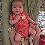 baby, infant, onesie, blanket, crib, plush_toy, sock, arm_motion, face, person, cute, lying_down, patterned_sheet, knit_blanket, indoor, child, newborn, soft_texture, colorful_background, portrait