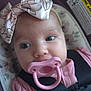 baby, pacifier, headband, car_seat, infant, closeup, pink, bow, child, face, eyes, clothing, seatbelt, warning_label, floral_pattern, young_child, cute, soft_lighting, indoors, portrait