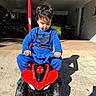 Jasper is registered to the contest to win money with this photo: child, toddler, boy, sitting, quad_bike, toy_vehicle, spiderman, marvel, outdoor, driveway, carport, sunlight, shadow, blue_clothing, red_vehicle, helmetless, portrait, playtime, car, brick_wall