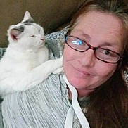 Iceee is registered to the contest to win money with this photo: woman, cat, glasses, smile, hoodie, indoor, couch, pet, white_cat, gray_markings, relaxing, affection, shoulder, long_hair, casual, portrait, friendship, comfort, cozy, home