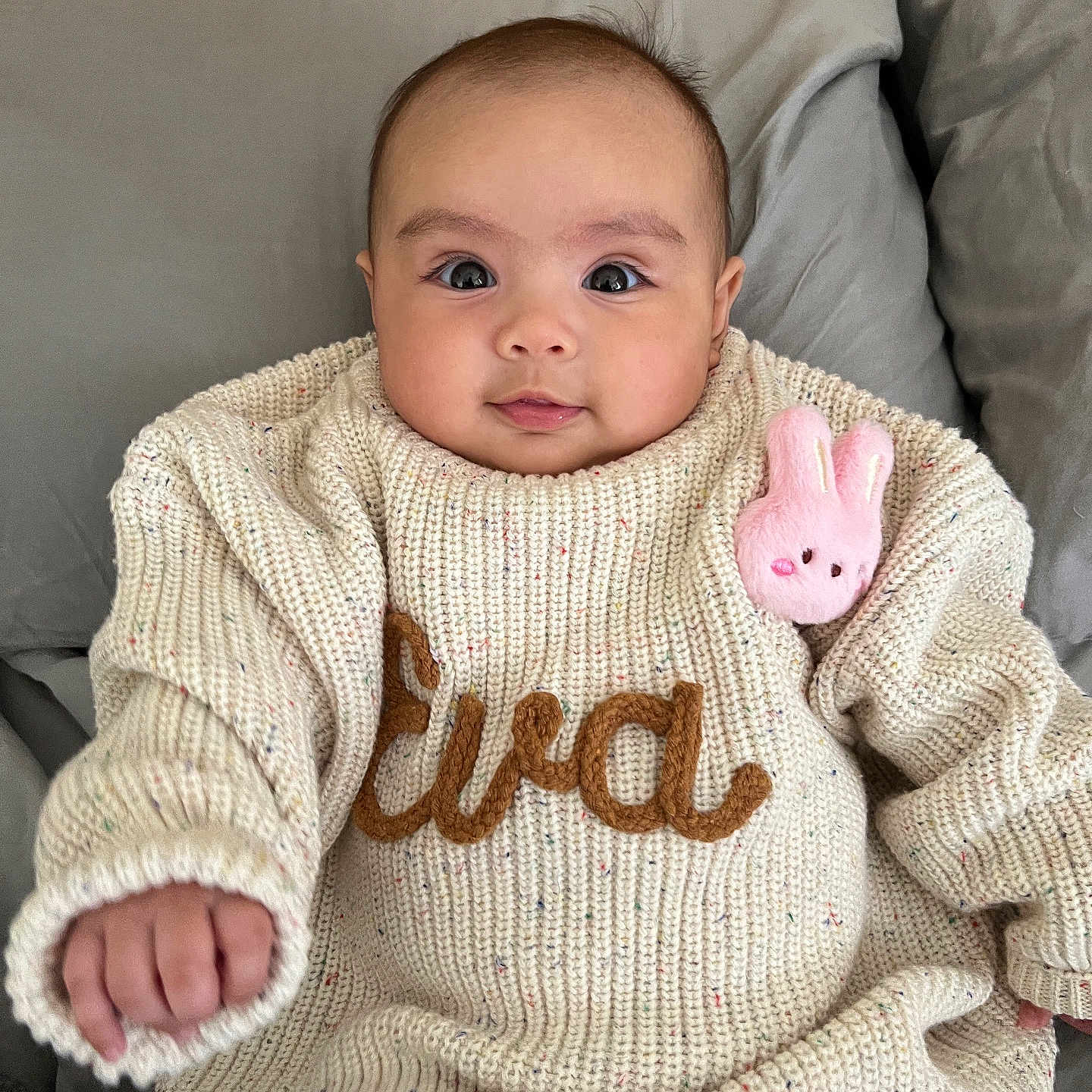 Eva Amelia joined the competition — help win amazing prizes! baby, child, infant, sweater, knitwear, plush_toy, pink, cute, portrait, face, smile, hand, cozy, indoors, fabric, couch, pillow, person, young, warm