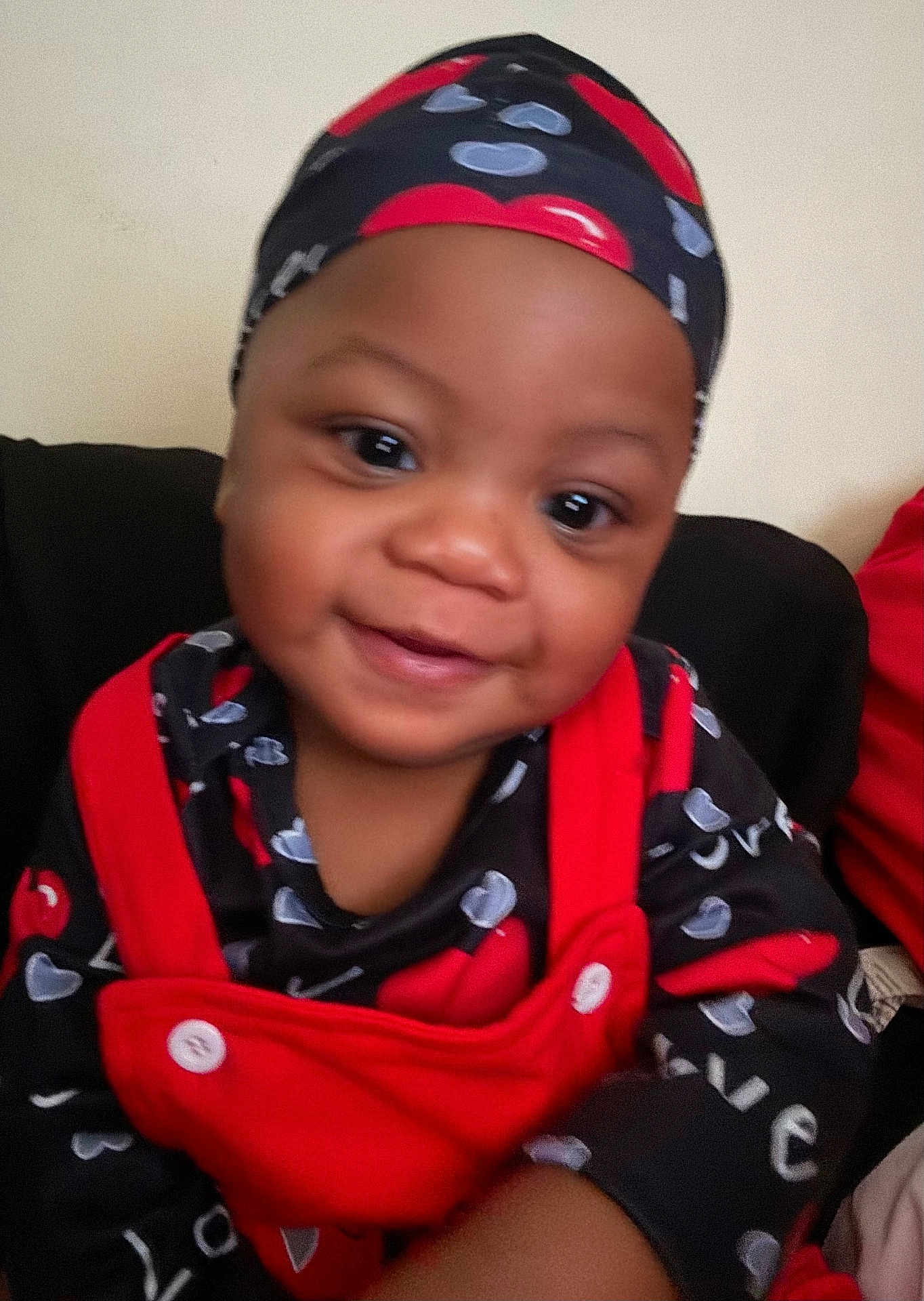 Donavyn is registered to the contest to win money with this photo: baby, child, smiling, red_clothing, black_clothing, headwear, indoor, portrait, cute, face, happy, young_child, infant, love_pattern, fabric, button, person, closeup, seated, warmth