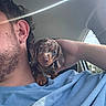 puppy, dog, person, shoulder, car, blue_shirt, earring, sunlight, cute, pet, animal, portrait, closeup, curious, indoor, casual, beard, hand, window, daylight