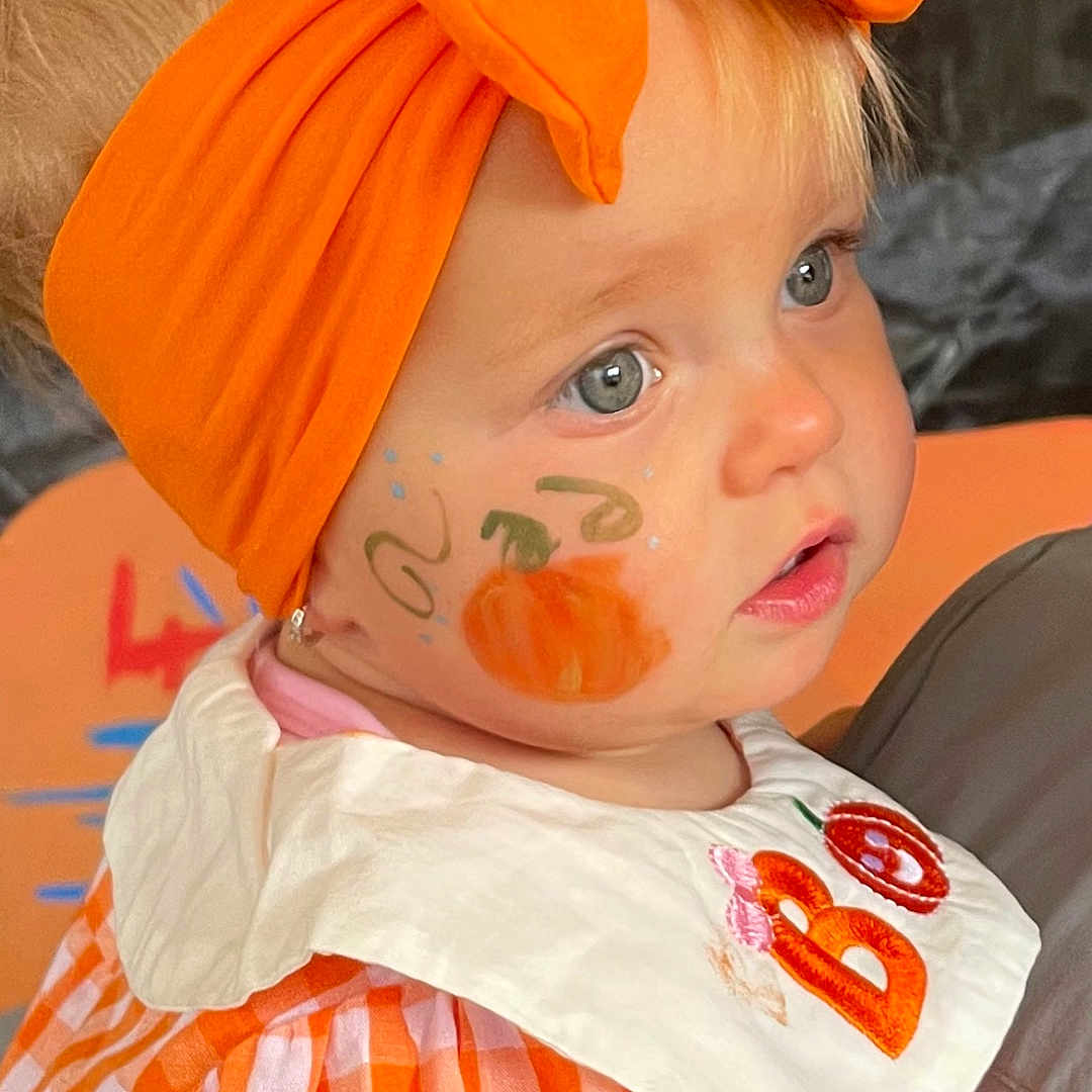 Saskiia is registered to the contest to win money with this photo: bow, child, close_up, costume, cute, embroidery, expression, face_paint, gingham_dress, halloween, holiday, indoor, orange_headband, person, portrait, pumpkin_paint, smile, soft_light, toddler, white_collar