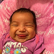 Ivry is registered to the contest to win money with this photo: baby, blanket, child, close_up, clothing, crib, face, floral_pattern, flowers, happy, indoors, infant, mattress, onesie, pink, portrait, purple, sleeping_area, smiling, tongue_out
