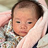 newborn, baby, infant, child, face, portrait, eyes, hair, blanket, pink_blanket, floral_clothing, swaddled, close_up, indoors, soft_lighting, pastel_colors, serious_expression, bedding, cozy, photography