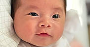Anly is registered to the contest to win money with this photo: baby, newborn, infant, child, face, portrait, close_up, wide_eyes, eyes, nose, mouth, dark_hair, white_clothing, onesie, swaddled, bedding, blanket, indoors, lying_down, photography