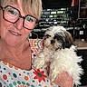 woman, person, dog, shih_tzu, pet, portrait, selfie, smiling, glasses, braces, blonde_hair, fluffy_fur, white_fur, black_and_white, holding_pet, colorful_sweater, kitchen, home, indoor, companion_animal