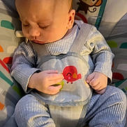 Zachary is registered to the contest to win money with this photo: baby, infant, child, sleeping, seated, activity_seat, bib, striped_clothing, blue_clothing, hands, face, portrait, cartoon_monkey, toy, colorful_background, indoor, nursery, highchair, baby_gear, photograph