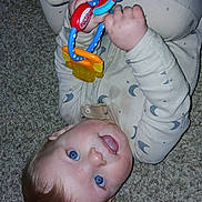 Isaac is registered to the contest to win money with this photo: baby, child, pajamas, toy, carpet, blue_eyes, infant, lying_down, hand, face, skin, hair, cute, indoor, play, expression, person, sleepwear, childhood, floor