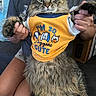 cat, tabby_cat, pet, animal, fur, clothing, shirt, person, hands, indoor, couch, seated, cute, funny, expression, holding, text, yellow_shirt, domestic_animal, closeup
