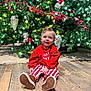 baby, child, christmas_tree, holiday, festive_clothing, red_sweater, striped_pants, wooden_floor, smiling, indoors, decorations, berries, greenery, ornaments, boots, cute, sitting, portrait, celebration, seasonal