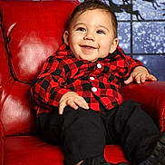 Sebastian is registered to the contest to win money with this photo: baby, child, smiling, red_chair, checkered_shirt, black_pants, black_shoes, indoor, portrait, holiday_theme, reindeer_silhouette, moon, winter_background, cute, happy, seated, infant, fashion, cozy, festive