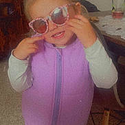 Mia participe au concours pour gagner de l'argent avec cette photo : child, cozy, cute, floor, furniture, glass, hair_tied, happy, indoor, long_sleeves, pants, person, photography, playful, portrait, purple_clothing, smiling, sunglasses, table, vest