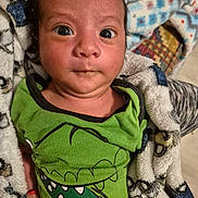 Miriam joined the competition — help win amazing prizes! baby, infant, child, face, eyes, blanket, clothing, green_shirt, dinosaur_print, expression, cute, portrait, indoor, person, newborn, skin, hand, closeup, young, soft_fabric