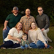 Samantha is registered to the contest to win money with this photo: family, outdoor, grass, smiling, casual_clothing, adult, child, group, portrait, nature, happy, people, trees, sitting, kneeling, daylight, greenery, jeans, plaid_shirt, glasses
