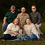 family, outdoor, grass, smiling, casual_clothing, adult, child, group, portrait, nature, happy, people, trees, sitting, kneeling, daylight, greenery, jeans, plaid_shirt, glasses