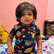 Arsh a rejoint le concours — aidez-le/la à gagner de superbes lots ! bed, blanket, bracelets, child, colorful_clothing, curly_hair, cute, furniture, indoor, looking_at_camera, pink_wall, portrait, rings, rocket_pattern, room, short_sleeves, sitting, stars, toddler, young_child