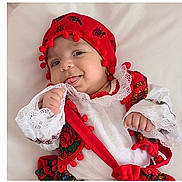 Ella Mary participe au concours pour gagner de l'argent avec cette photo : baby, child, traditional_clothing, red_hat, pom_poms, white_lace, smiling, tongue_out, cute, adorable, infant, portrait, cultural, colorful, hand, face, happy, soft_background, clothing, person