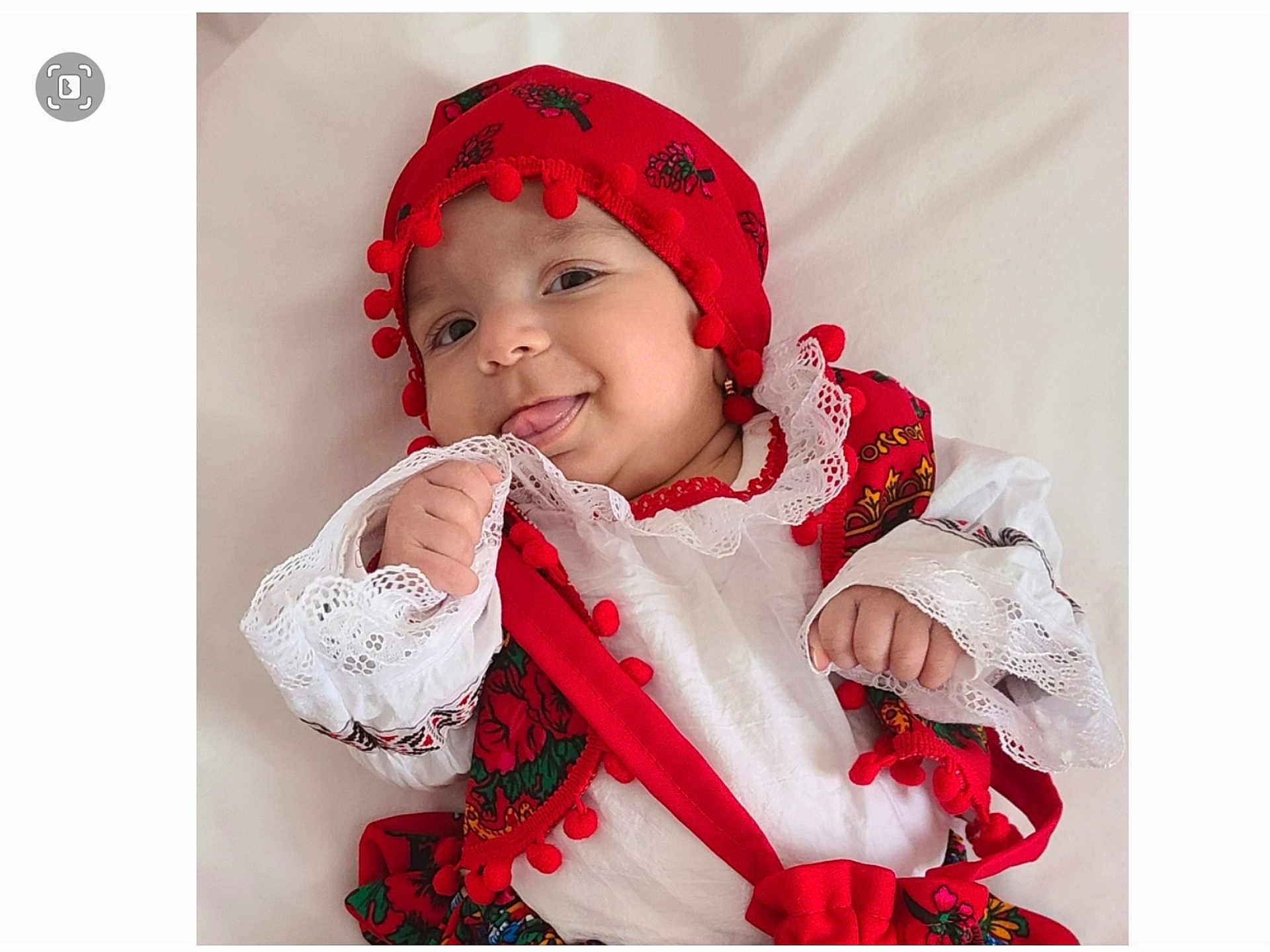 Ella Mary participe au concours pour gagner de l'argent avec cette photo : baby, child, traditional_clothing, red_hat, pom_poms, white_lace, smiling, tongue_out, cute, adorable, infant, portrait, cultural, colorful, hand, face, happy, soft_background, clothing, person