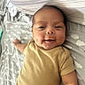 baby, infant, smiling, onesie, bed, pillow, blanket, sleepwear, child, cute, happy, lying_down, face, skin, head, arm, indoors, person, newborn, resting
