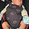 baby, sleeping, car_seat, mittens, dinosaur_outfit, infant, cute, child, peaceful, clothing, seatbelt, mickey_mouse_pattern, soft_lighting, indoors, newborn, portrait, resting, adorable, cozy, tiny